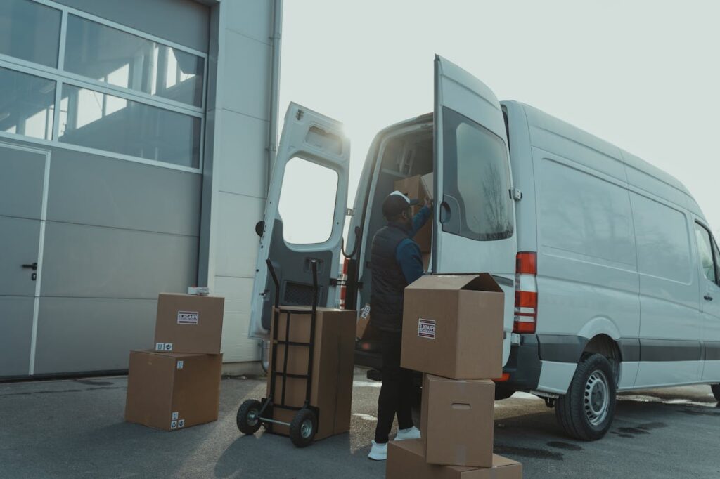 pexels-photo-6169177 Courier loading cardboard boxes into a delivery van outside a warehouse.
